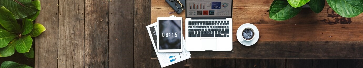 image of a wooden desk with a coffee cup, laptop and tablet.